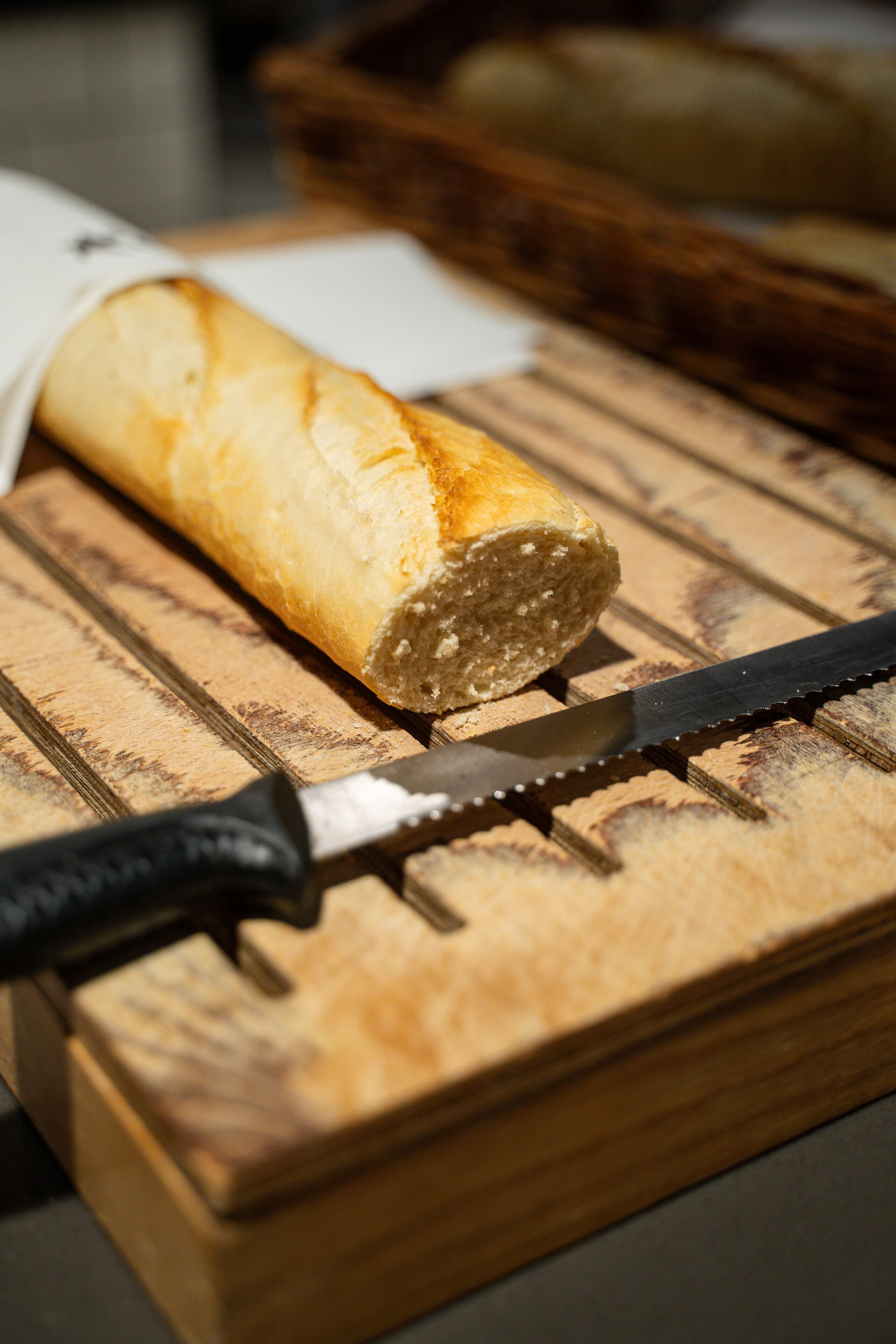 Ein Baguette auf einem Holztisch mit einem Messer daneben.