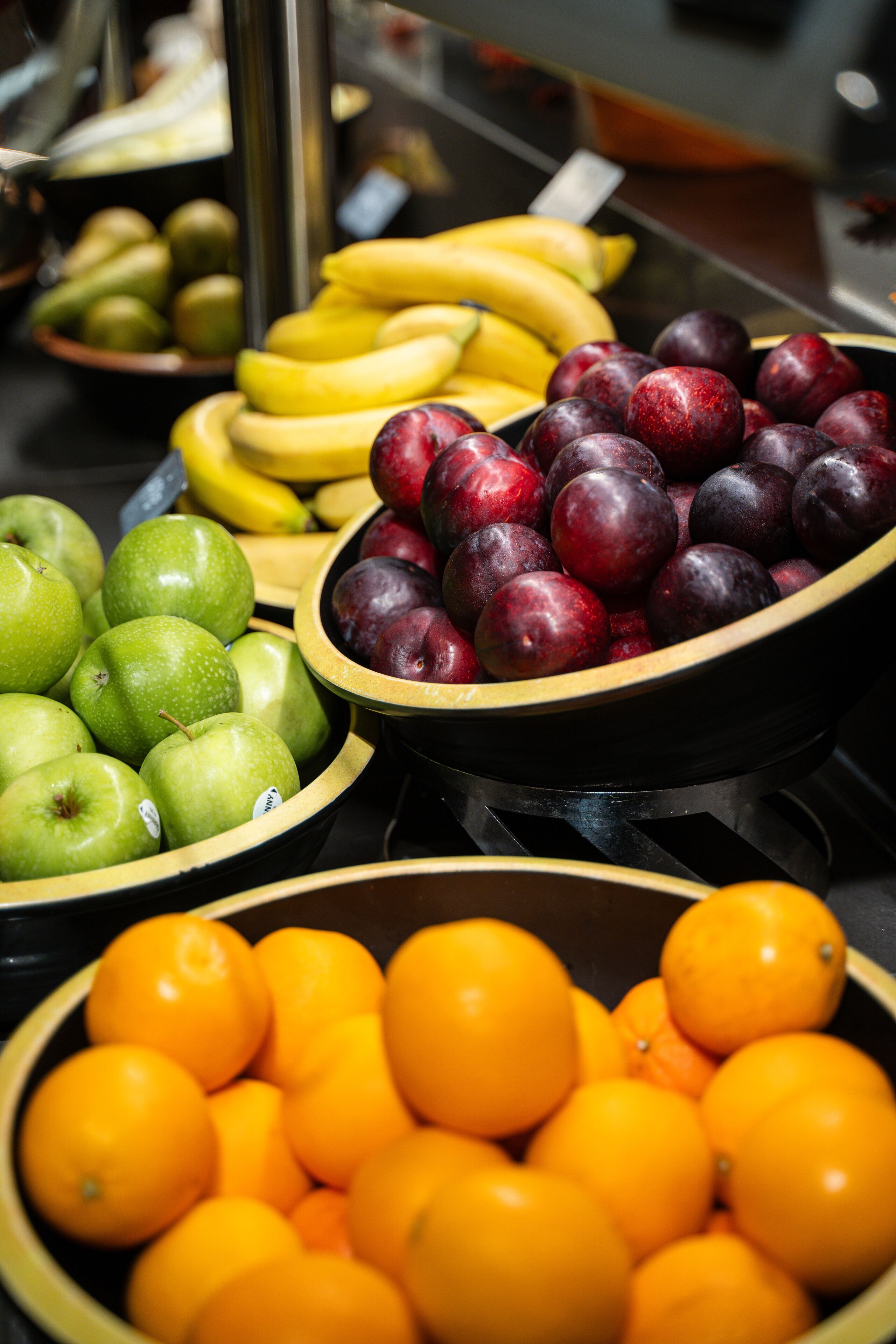 A display of various fruits including apples, bananas, plums, and oranges.