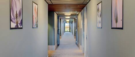 A hallway with framed floral artwork on the walls, a patterned carpet, and a ceiling with recessed lighting.