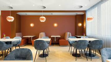 Zona pranzo moderna con tavoli rotondi e sedie grigie, posti a sedere arancioni e illuminazione a sospensione.