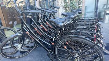 A row of bicycles parked in an outdoor area with a glass wall in the background.