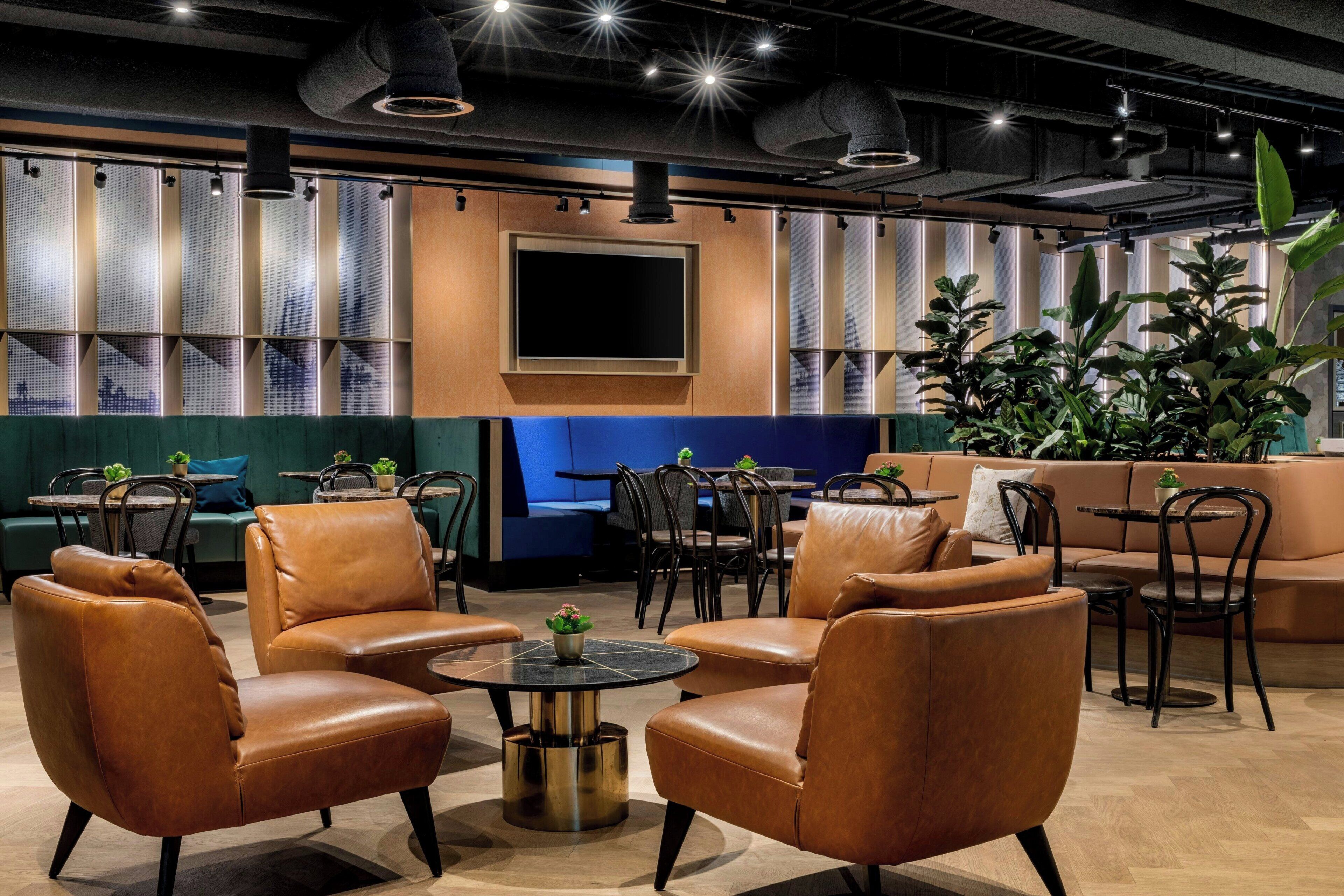 Un'area lounge moderna con divani in pelle, tavoli rotondi e piante in vaso.