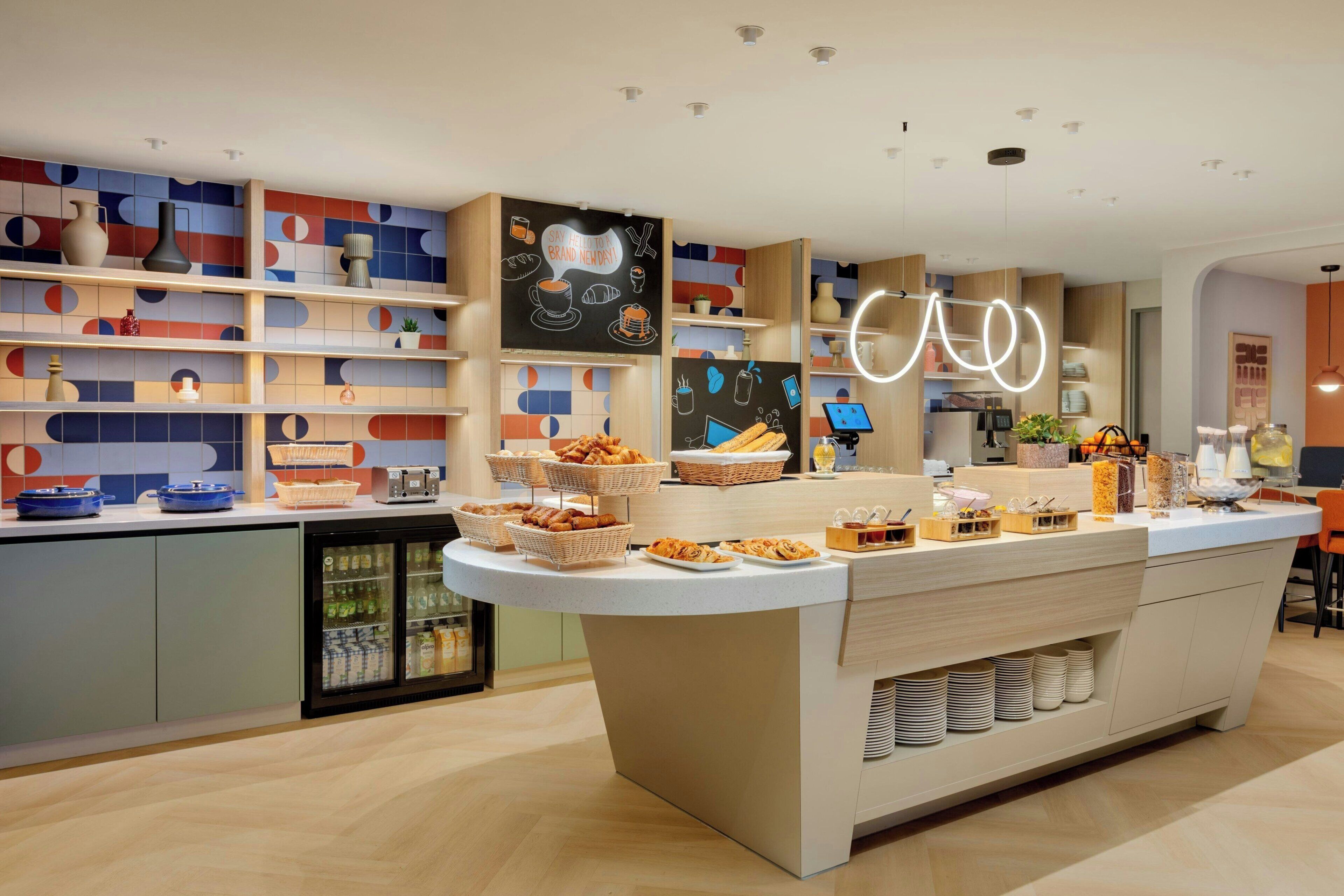 A modern cafe with a central counter, shelves with various items, and a wall with a chalkboard sign.