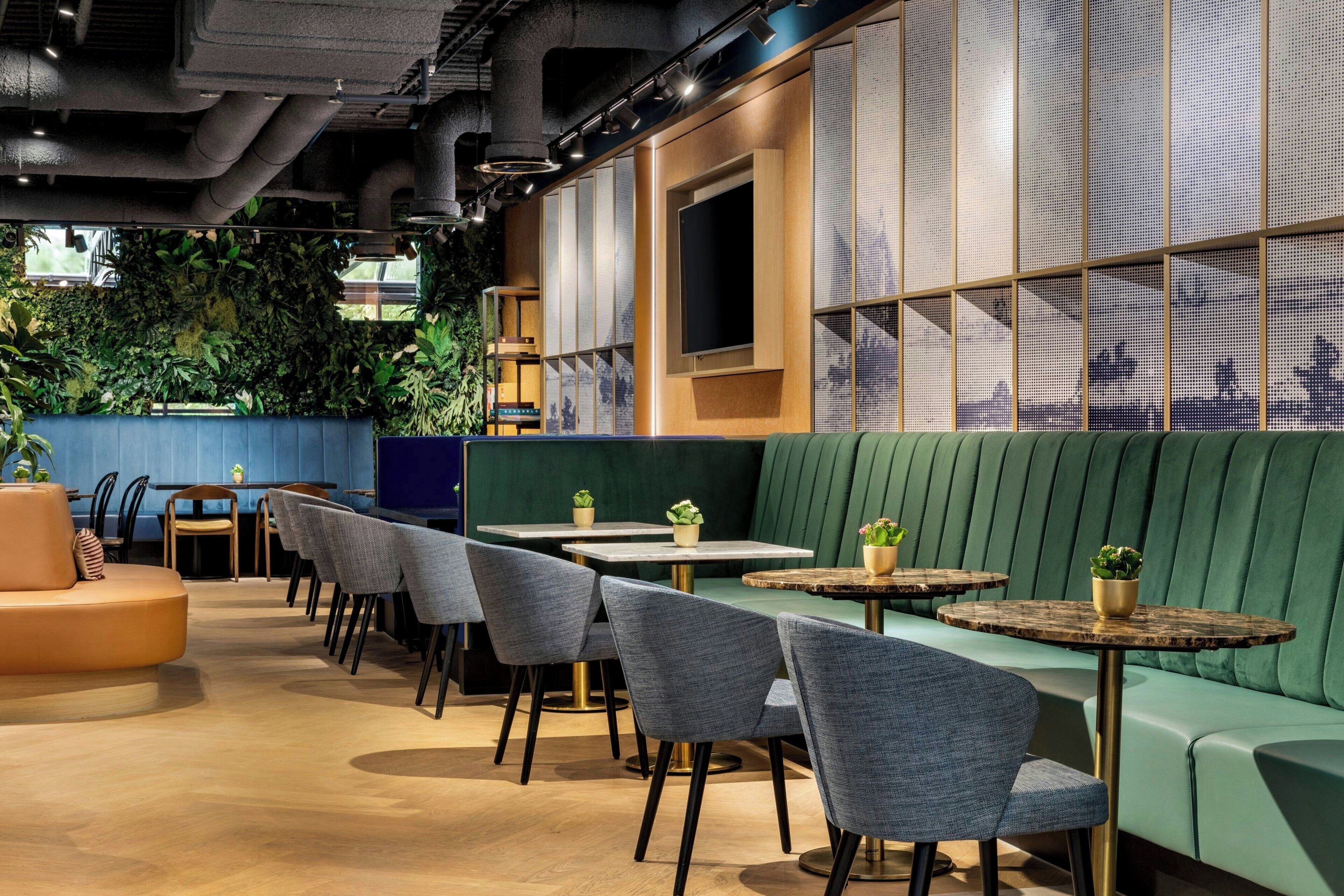 Un intérieur de restaurant moderne, avec des espaces aménagés pour les clients, des tables et un mur végétal orné de plantes.