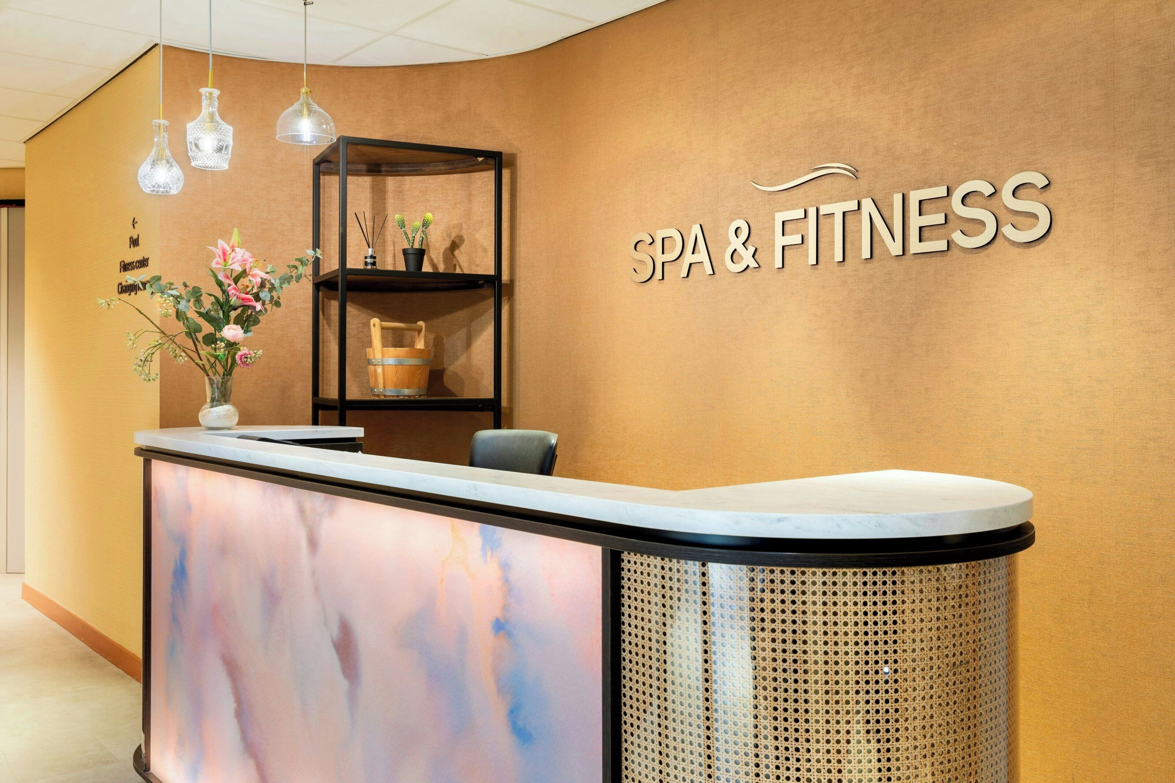 Una reception con piano in marmo, una insegna a parete che recita 'SPA & FITNESS' e uno scaffale con oggetti decorativi.