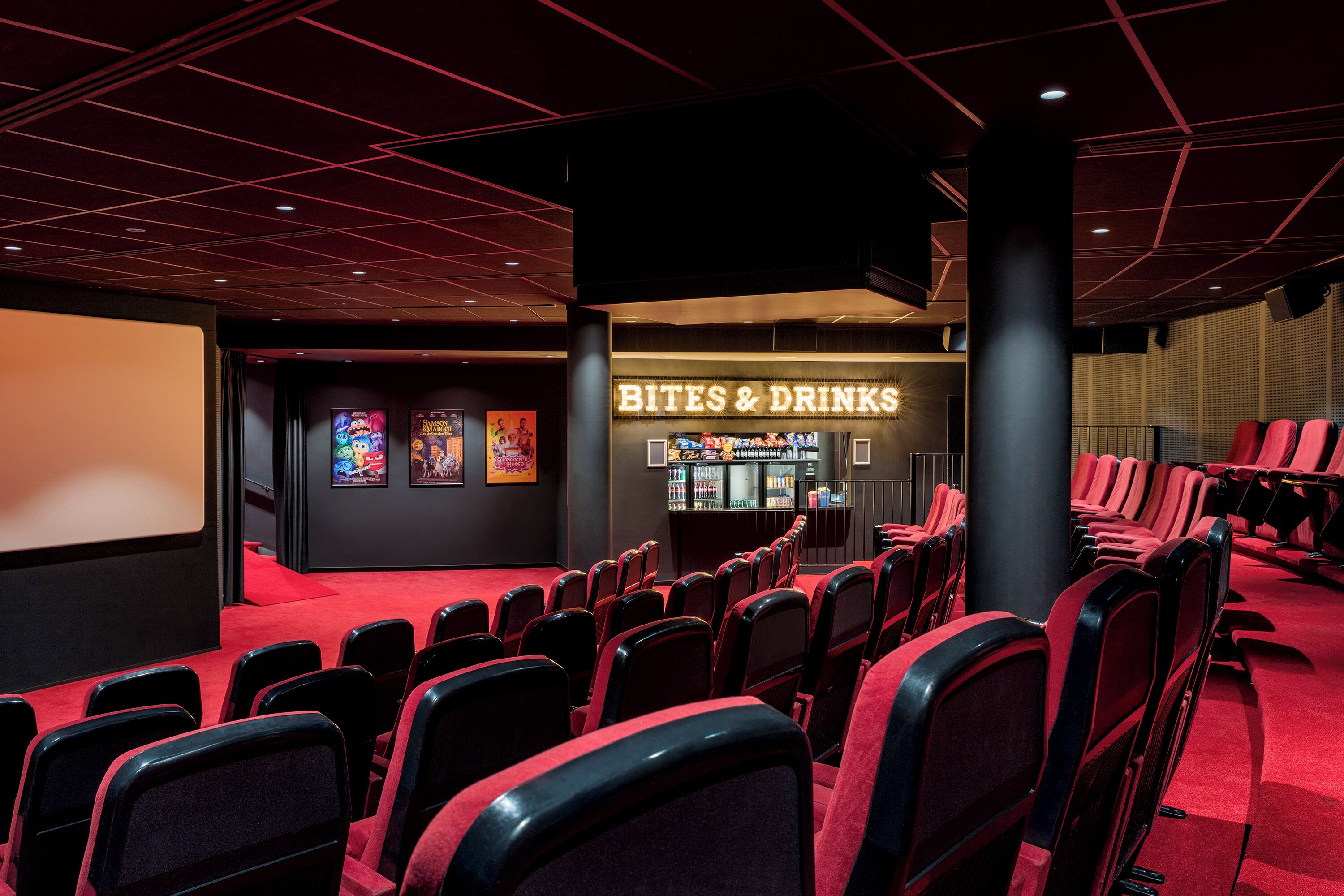 A cinema with rows of red seats, a 'Bites & Drinks' counter, and framed movie posters on the wall.