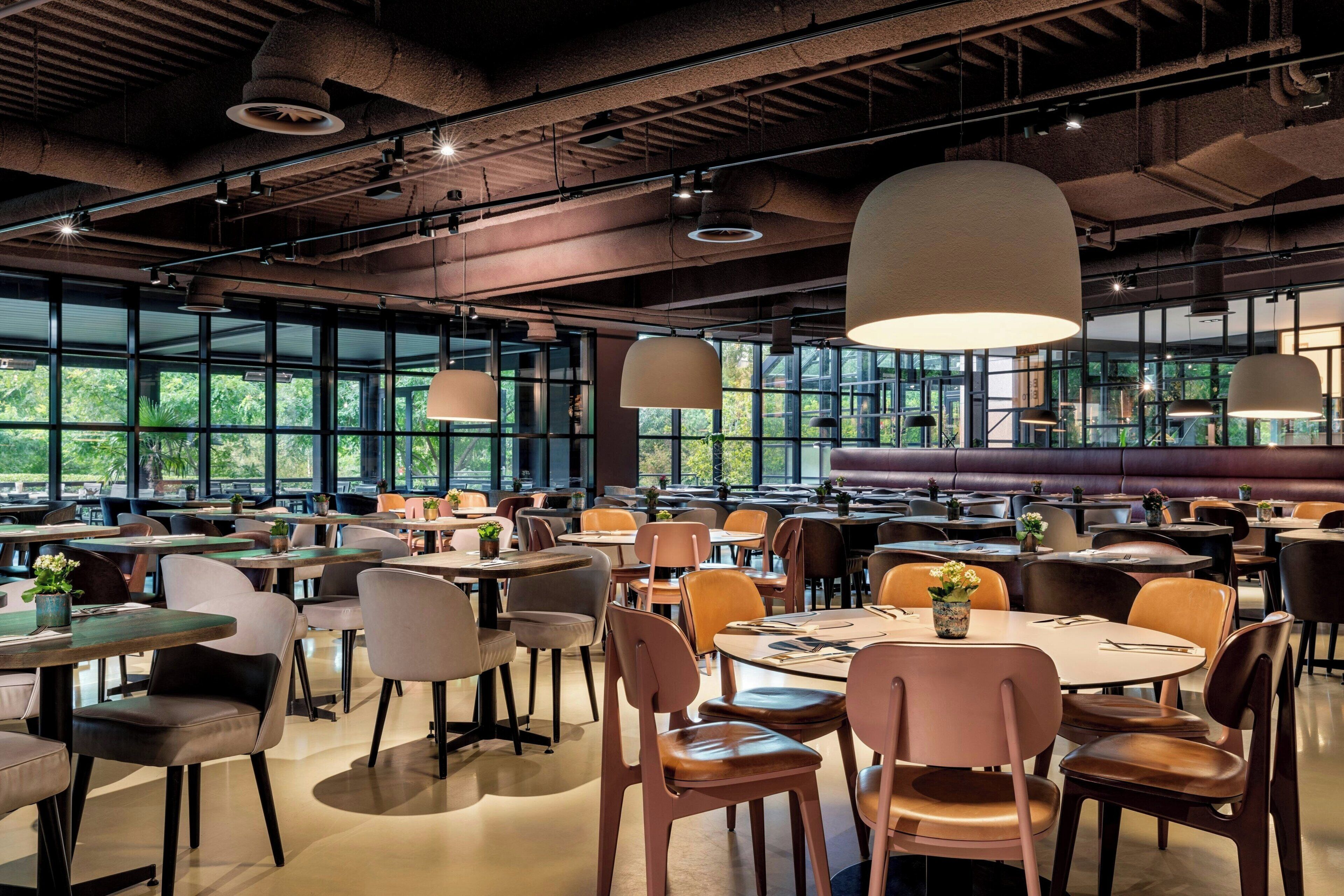 En rymlig restaurang med högt i tak, stora fönster och modern belysning.