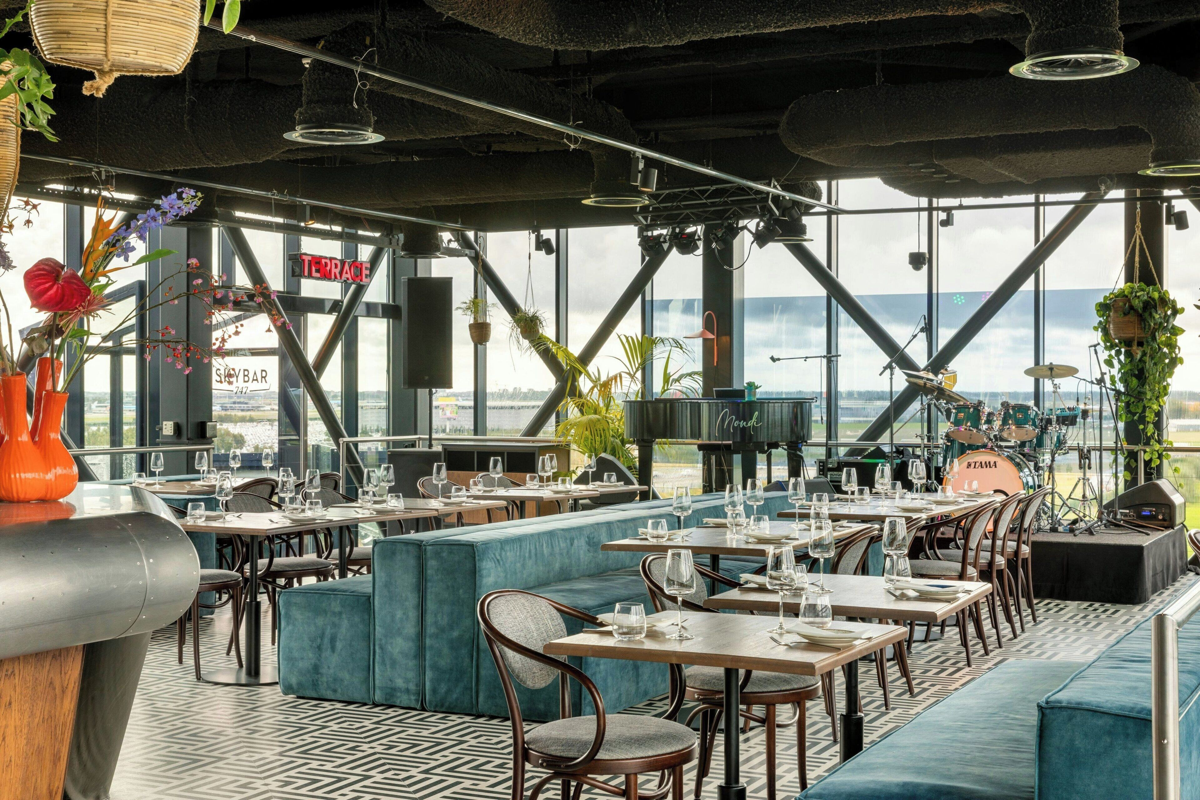 A restaurant with tables and chairs, a stage with musical instruments, and a view of the city.