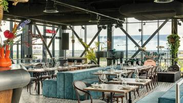 A restaurant with tables and chairs, a stage with musical instruments, and a view of the city.