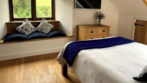A bedroom with a bed, a window with a view, a dresser, and a TV mounted on the wall. - Barn and Stables in tranquil gardens and farmland (Boscastle)