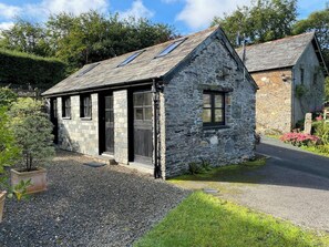 A stone cottage with a sloped roof, a small porch, and a gravel driveway.
