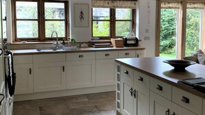 A kitchen with white cabinets, a sink, a toaster, and large windows offering a view of greenery. - Barn and Stables in tranquil gardens and farmland (Boscastle)