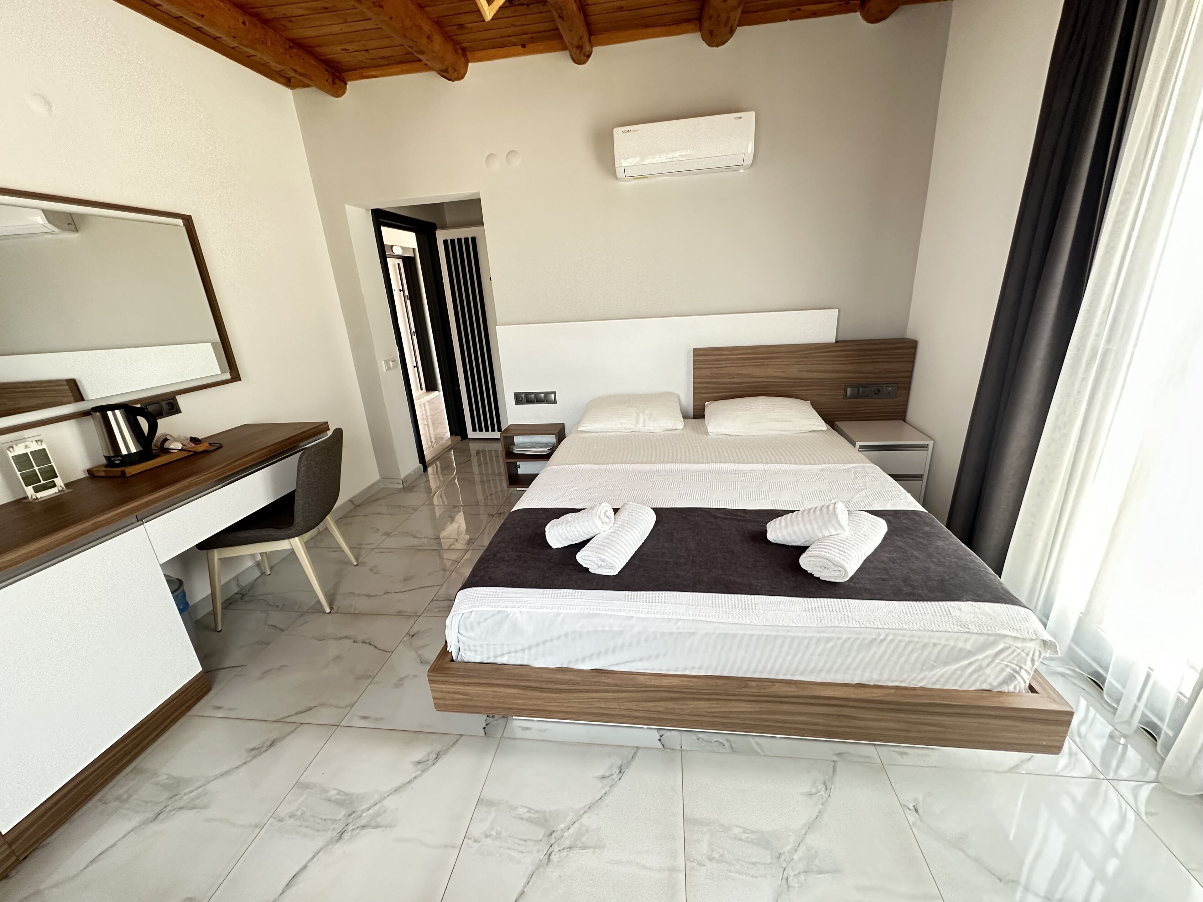 A modern hotel room with a bed, a desk, a chair, and a large mirror.