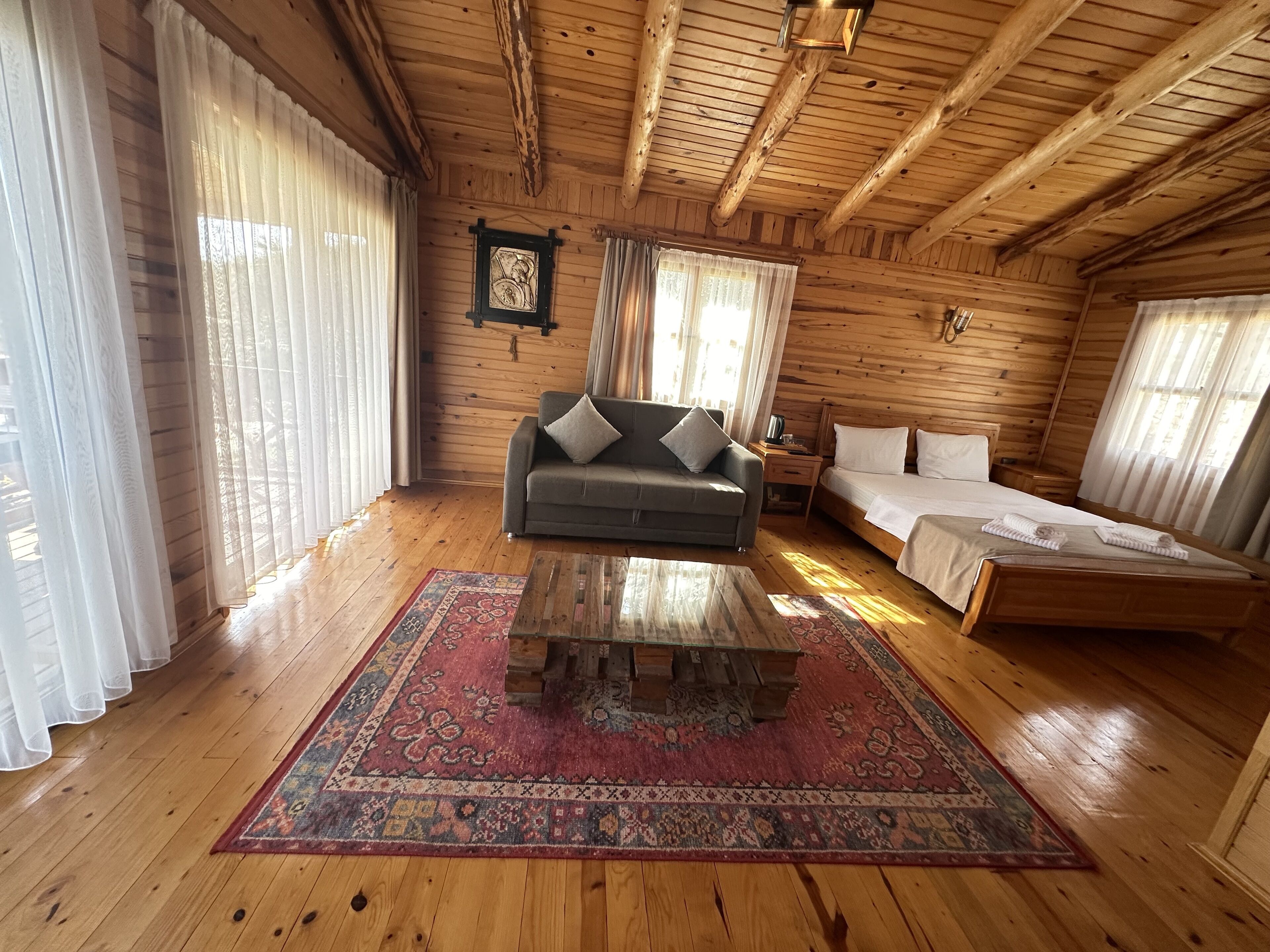 A wooden cabin interior with a sofa, a bed, a nightstand, and a patterned rug.