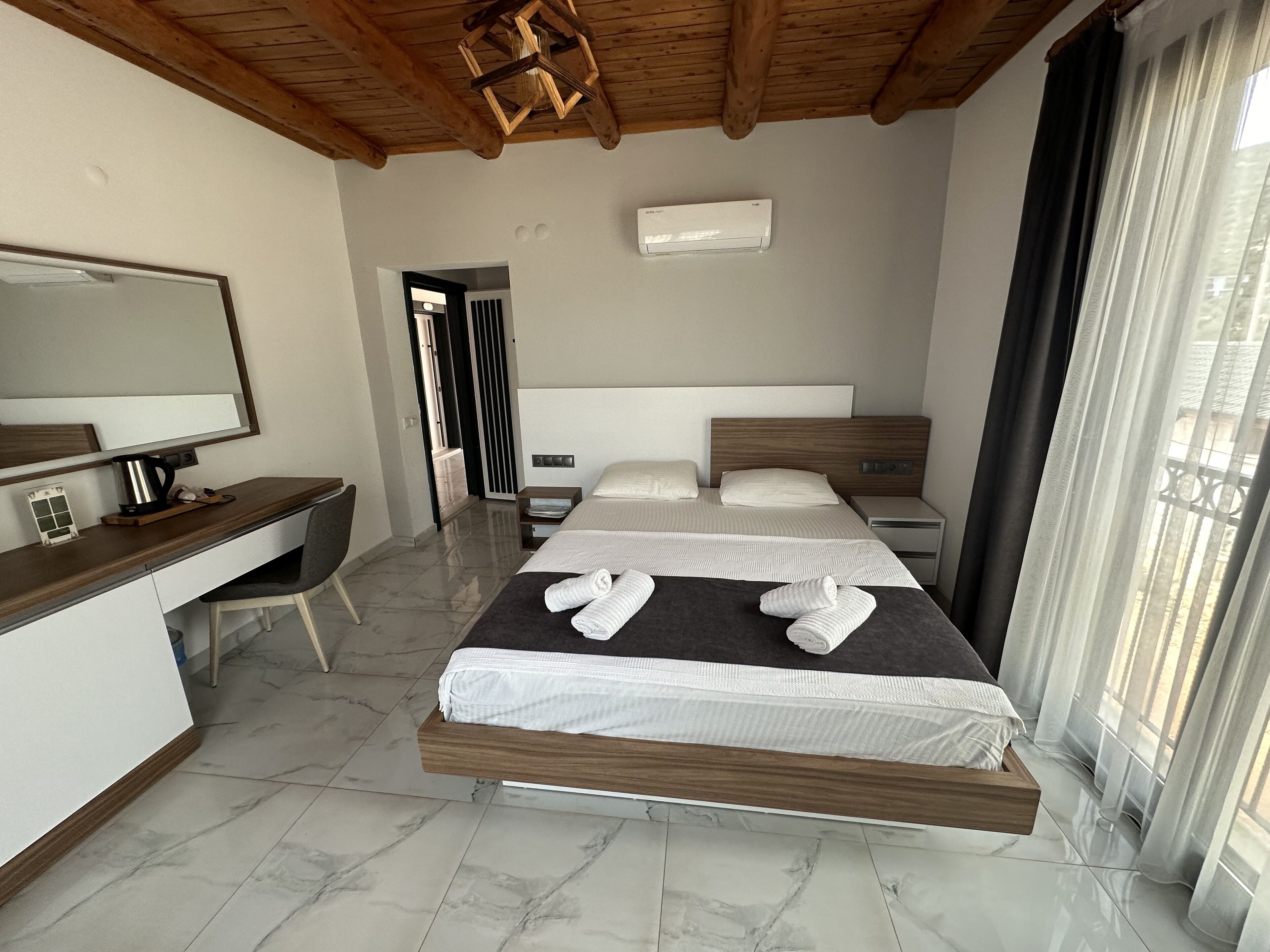 Ein modernes Hotelzimmer mit Bett, Nachttischen, Schreibtisch, Stuhl, Spiegel und einem fenster mit Vorhängen.