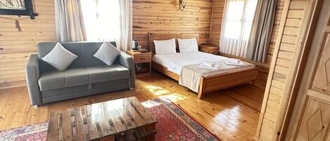 A wooden cabin interior with a sofa, a bed, a wooden coffee table, and a patterned rug.