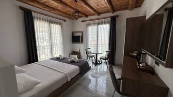 Habitación de hotel con cama, escritorio, silla, televisión y ventanas amplias.