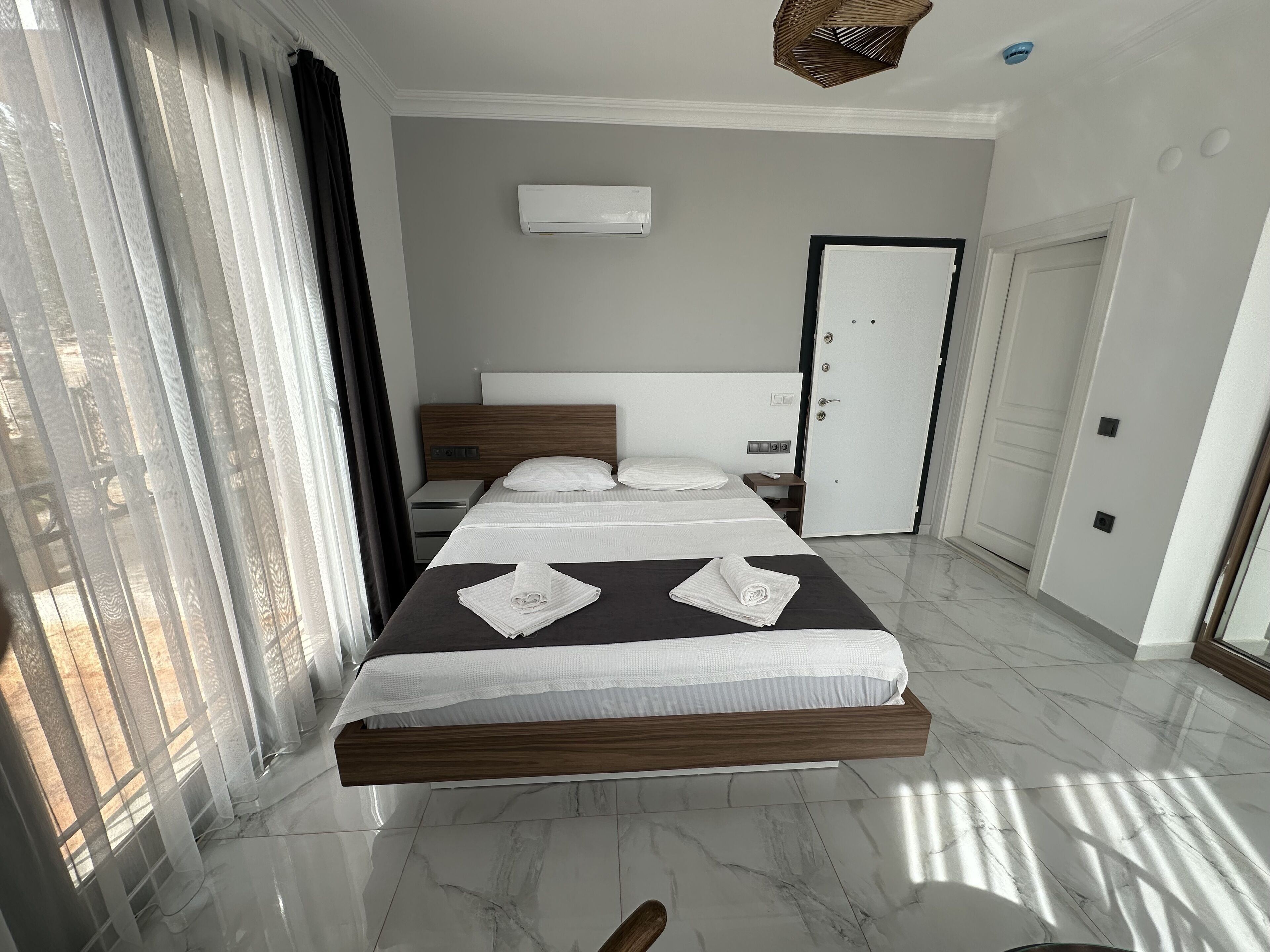 Habitación de hotel moderna con una cama grande, una mesita de noche, un armario y una ventana con cortinas.