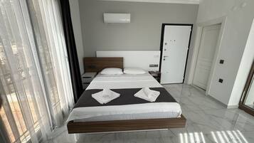 Habitación de hotel moderna con una cama grande, una mesita de noche, un armario y una ventana con cortinas.
