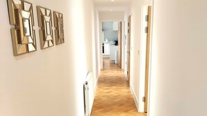 A hallway with a wooden herringbone floor, white walls, and three geometric wall art pieces.