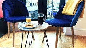 A cozy room with two blue chairs, a small round table, a glass of orange juice, a mug of dark liquid, and a plate of cookies.