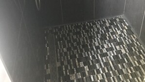Ein Duschbereich mit schwarzen Fliesen und einem gemusterten Boden.