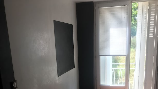 Ein Schlafzimmer mit einem Bett, einem kleinen runden Tisch, einem an der Wand befestigten Fernseher und einem Fenster mit Jalousien.