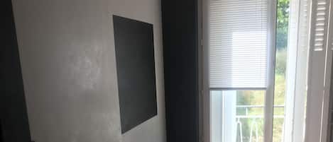 A bedroom with a bed, a small round table, a wall-mounted TV, and a window with blinds.