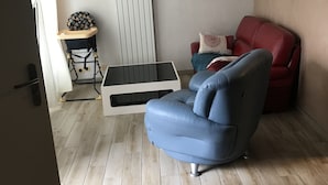 Ein Wohnzimmer mit einem blauen Sofa, einem roten Sessel, einem weißen Heizkörper und einem Babywippstuhl.