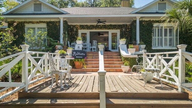 Ein Haus mit überdachter Veranda, weißen Geländern und Gartenmöbeln.