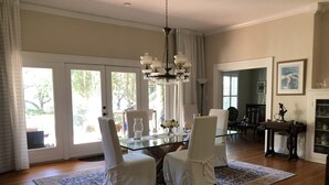 Ein Essbereich mit Glastisch, weißen Stühlen, einer Chandelierleuchtre und Blick durch große Schiebetüren.