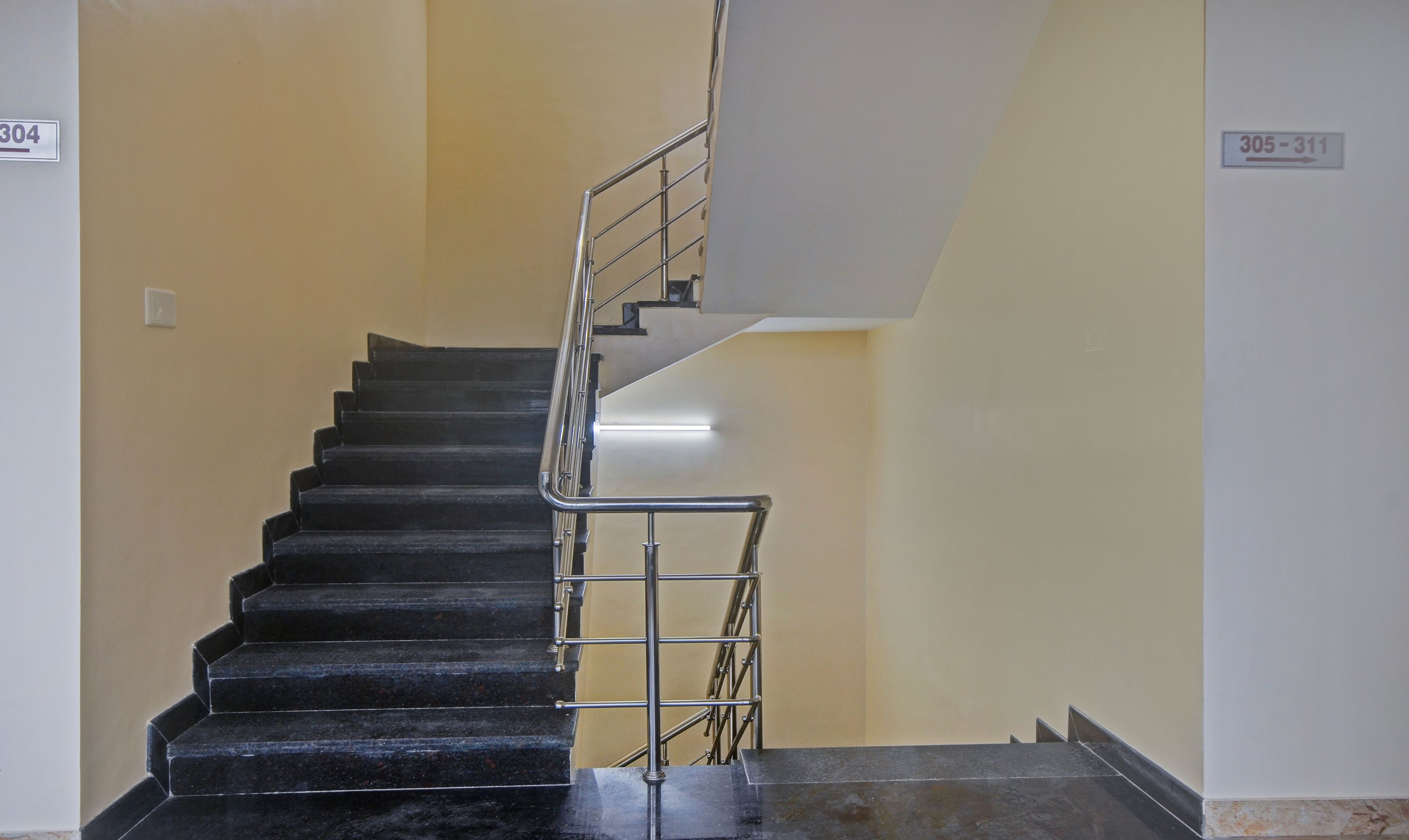 A staircase with black steps and a metal railing, leading to a landing with a light fixture.
