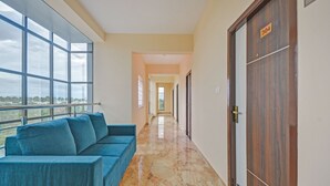 A corridor with a blue sofa, a wooden door with a number, and a view through large windows. - Treebo Everest Residency Tidel Park (Coimbatore)