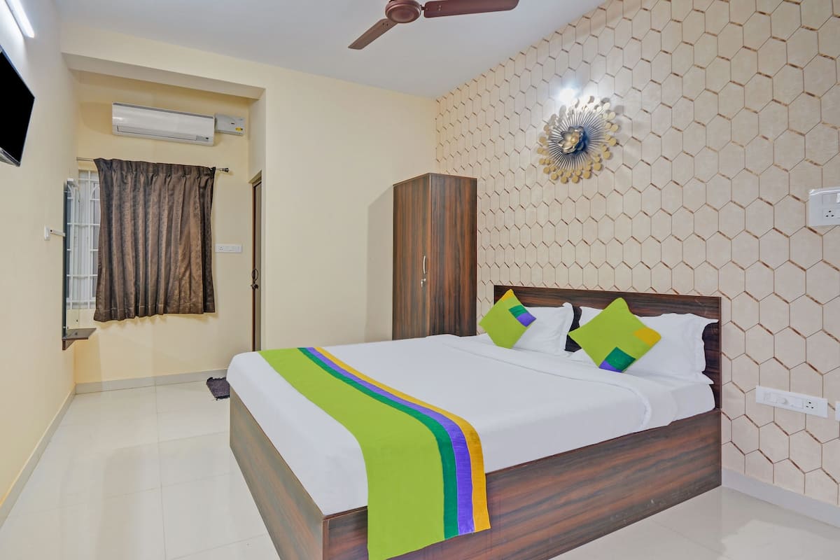 A hotel room with a bed, a wardrobe, an air conditioning unit, a ceiling fan, and a decorative wall panel.
