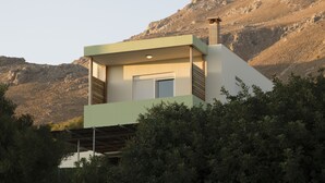 A modern house with a flat roof, a chimney, and a window with shutters. - Paterakis Studio's Triopetra (Agios Vasileios)