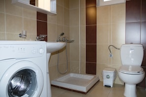 A bathroom with a washing machine, a sink, a toilet, and a shower.
