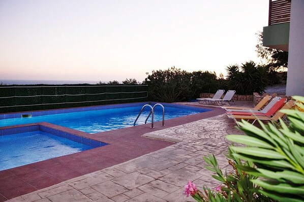 A swimming pool with a view of the ocean, surrounded by lounge chairs and a stone pathway.