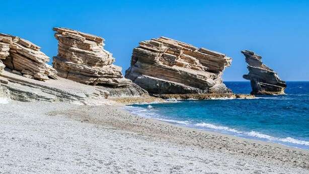 A rocky coastline with layered rock formations and a clear blue sea. - Paterakis Studio's Triopetra (Agios Vasileios)
