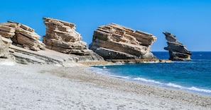 A rocky coastline with layered rock formations and a clear blue sea.