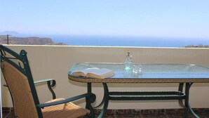 A glass table with a book and a bottle, a wicker chair, and a view of the ocean. - Paterakis Studio's Triopetra (Agios Vasileios)