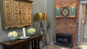 A living room with a brick fireplace, a wooden cabinet with floral carvings, a table with a vase of flowers, and a bookshelf. - Beautiful, artistic, unique and beyond large and spacious apartment (Little Falls)