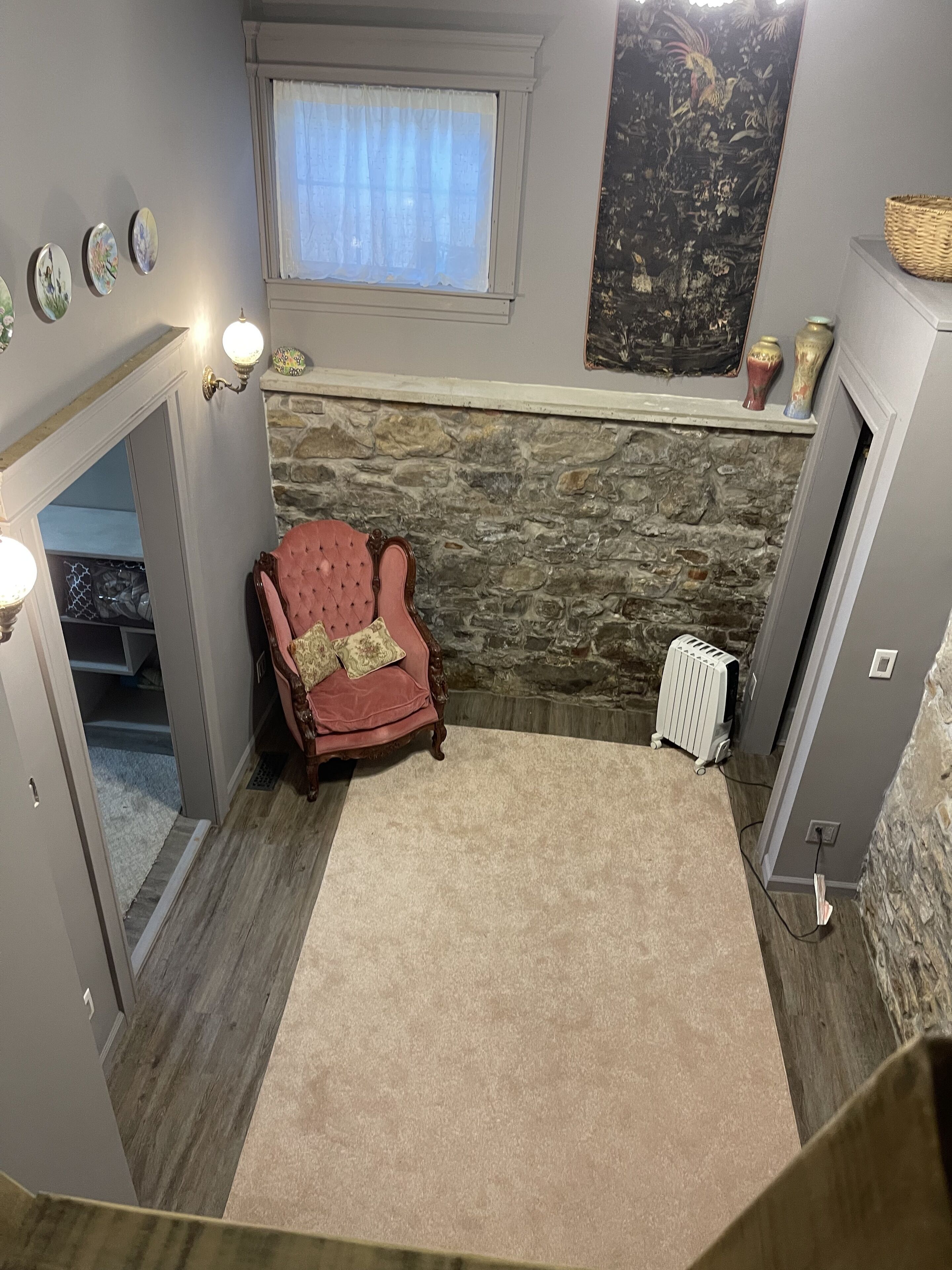 A cozy room with a stone wall, a red armchair, a small window with curtains, and a radiator.
