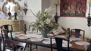 A dining area with a long table set for four, surrounded by chairs, with a chandelier above and a tapestry on the wall. - Beautiful, artistic, unique and beyond large and spacious apartment (Little Falls)
