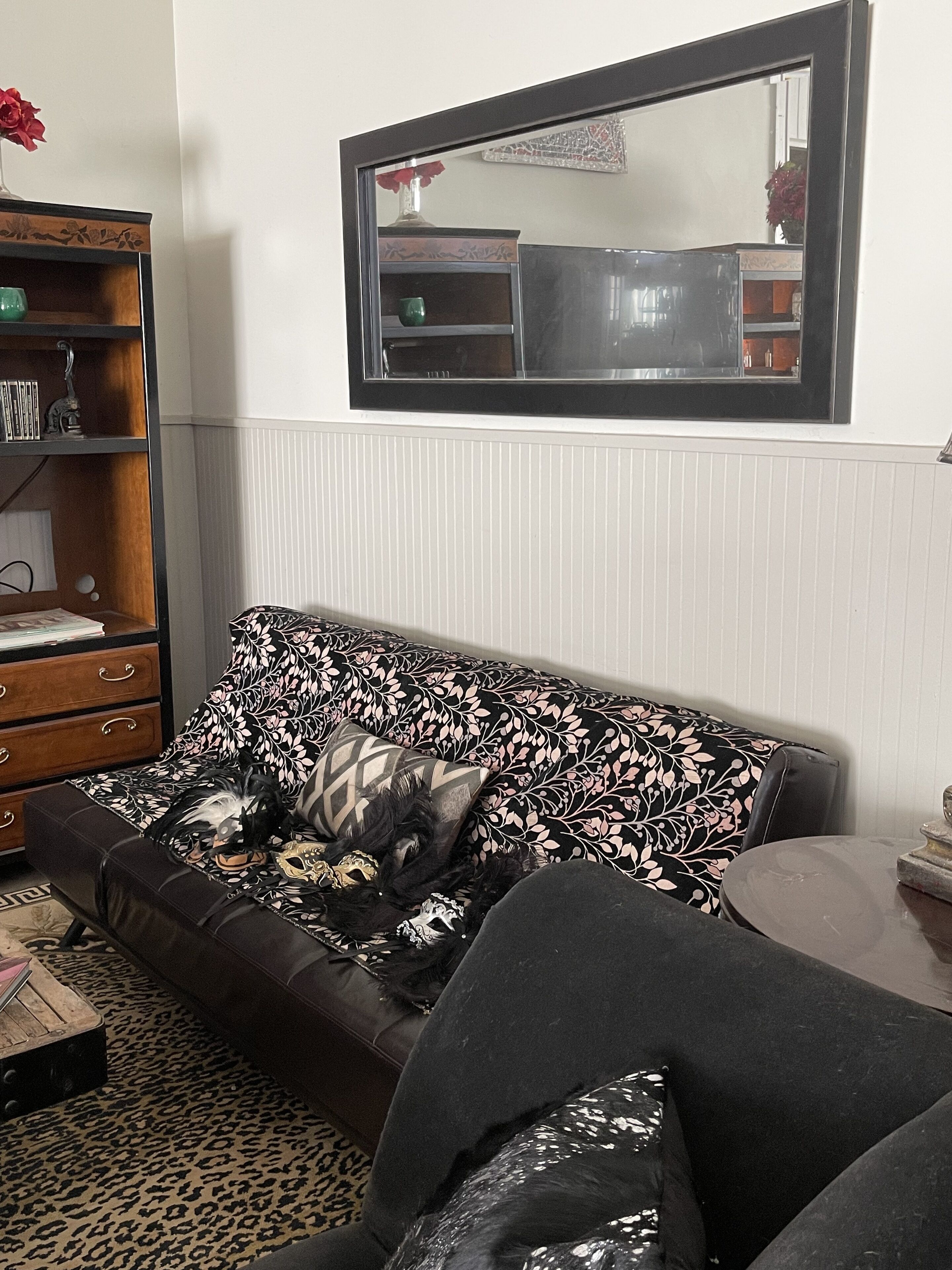 A living room with a patterned sofa, a wooden cabinet, and a mirror on the wall.