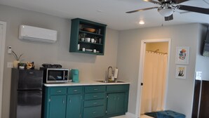 Una cocina compacta con gabinetes verde azulado, un refrigerador negro, un microondas y un ventilador de techo.