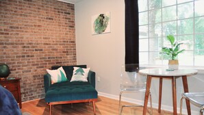 Una sala de estar con pared de ladrillo, un sofá verde, una mesa redonda y una planta en maceta.