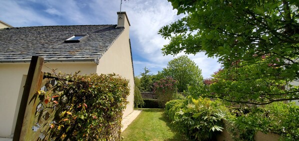 A house with a sloped roof, a small window, and a garden with various plants and a lawn.