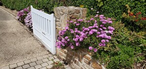 A white gate with a stone wall and flowering plants.