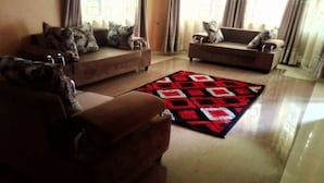 A living room with two sofas, a patterned rug, and a door in the background. - A & J Holiday Suites - Fort Portal (Bouvet Island)