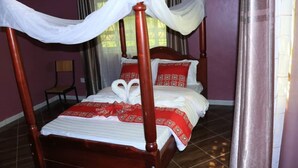 A four-poster bed with white and red bedding, a wooden headboard, and a canopy. - A & J Holiday Suites - Fort Portal (Bouvet Island)